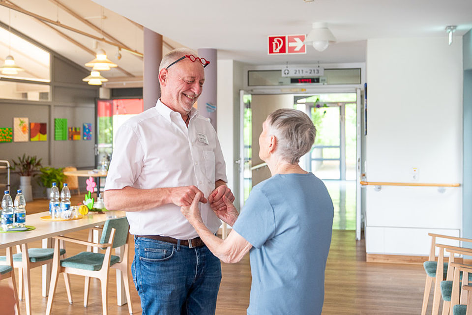 Ein Mitarbeiter der Pflegeeinrichtung tanzt mit einer Bewohnerin im Aufenthaltsraum.
